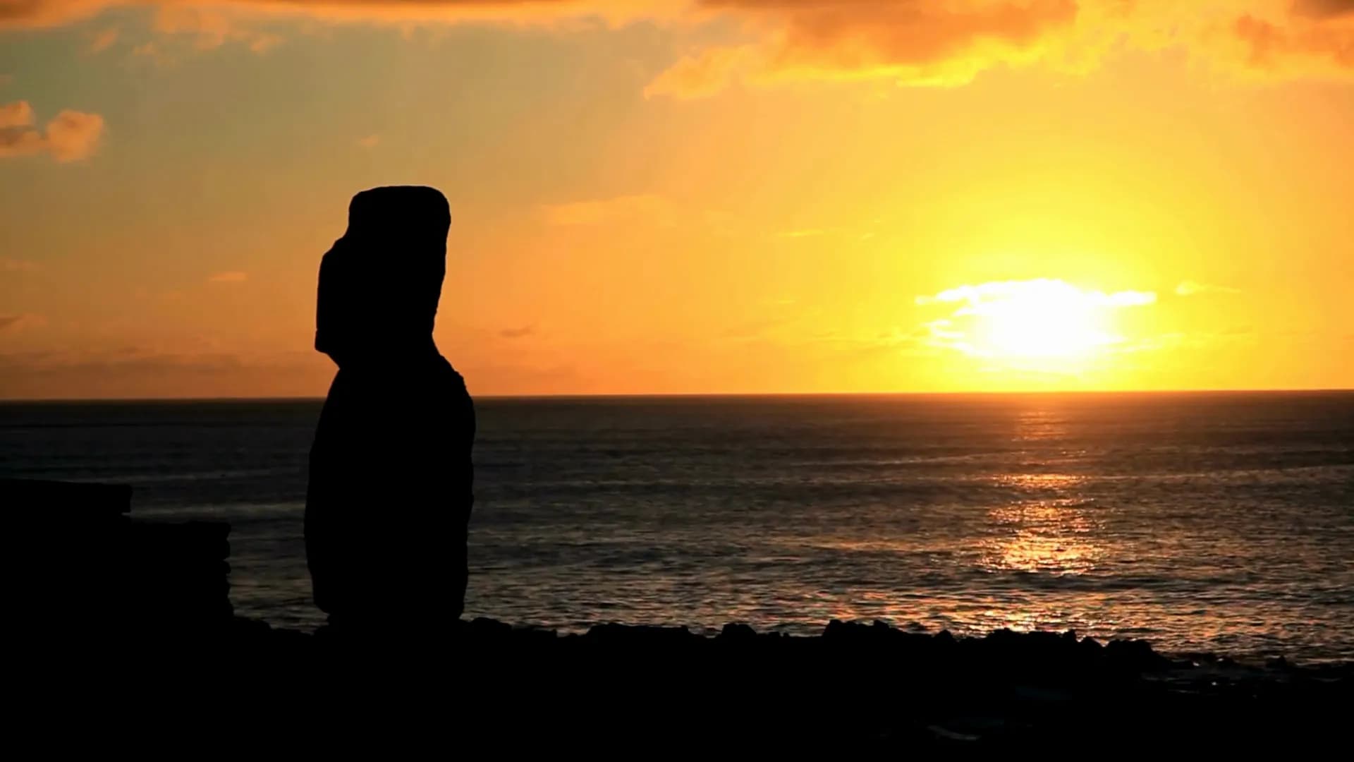 Silhueta de um moai contra o pôr do sol sobre o Pacífico