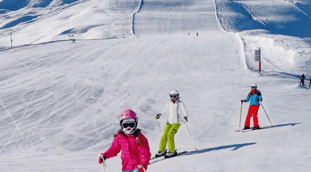 Criança esquiando com a família numa pista larga do Valle Nevado